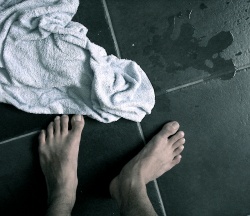 A towel and a pair of wet white feet on a tile bathroom floor